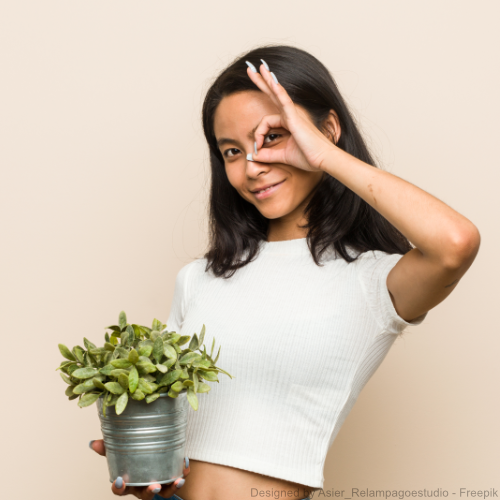 Eine Frau hält einen Blumentopf, in dem sich eine Pflanze befindet und formt mit der anderen Hand das Ok-Zeichen vor ihrem Auge