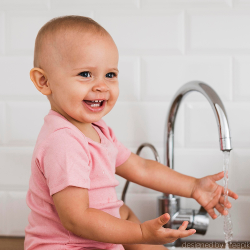 Ein Baby hält lächelnd die Hand unter einen Wasserhahn.