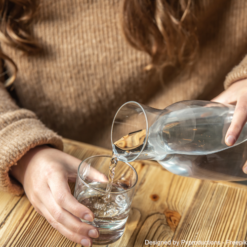 Eine Frau Füll Wasser aus einer Glaskaraffe in ein Wasserglas