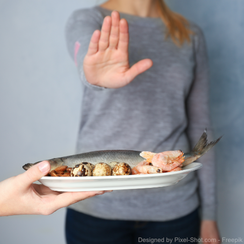 Eine Frau signalisiert mit ihrer Hand, dass sie den zubereiteten Fisch nicht essen will