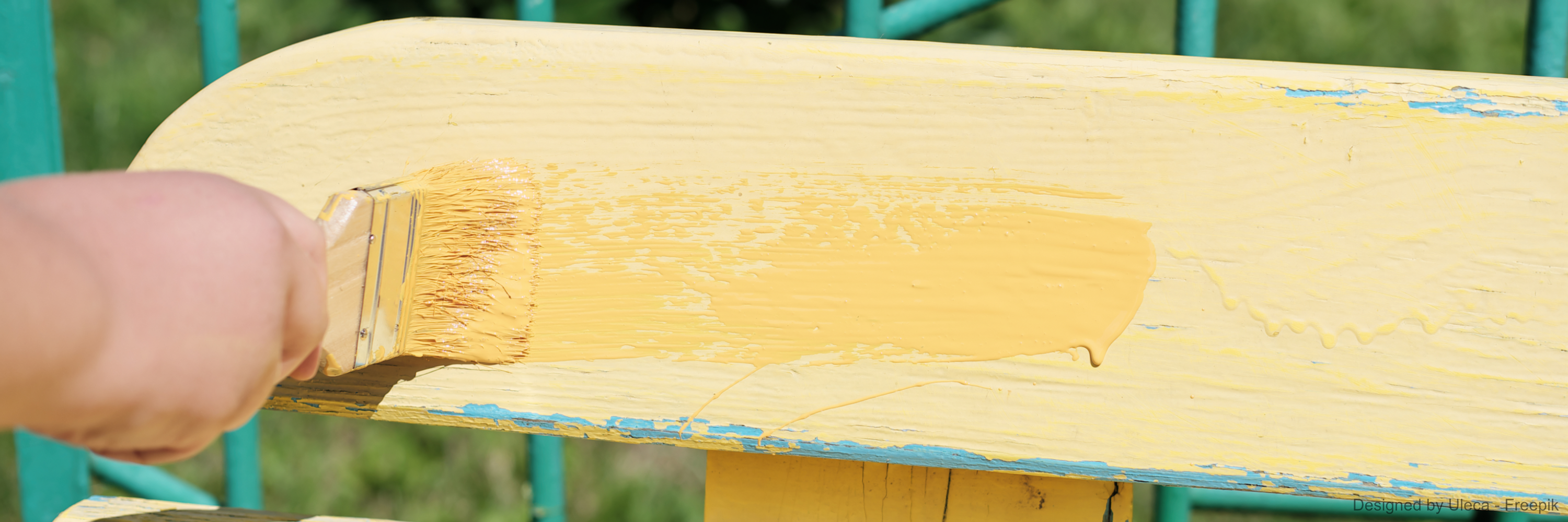 Eine Hand bestreicht eine Holzbank mit gelber Farbe