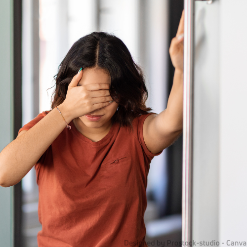 Eine Frau lehnt am Türrahmen und hält sich eine Hand vor die Augen, weil ihr schwindelig ist. 