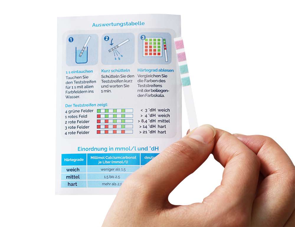 Hand hält einen Wasserhärte-Teststreifen vor die Auswertungstabelle mit Farbskala zur Bestimmung des Härtegrads.
