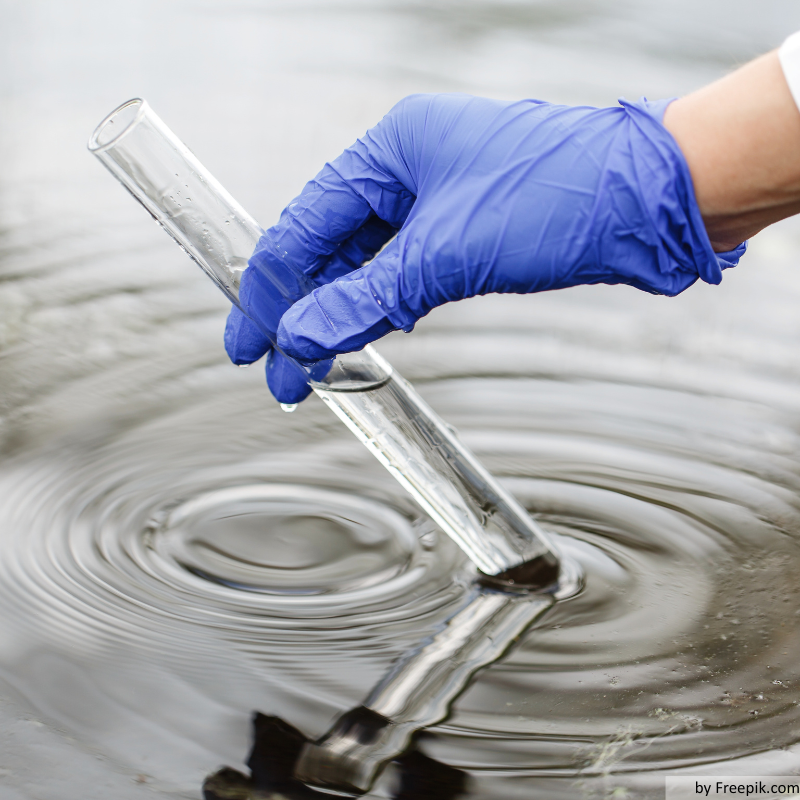 Forscher hält ein Reagenzrohr mit Wasser in einer Hand in blauem Handschuh.
