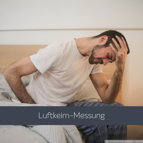Ein Mann sitzt im Schlafanzug auf einem Bett, beugt sich nach vorne und stützt seinen Kopf nachdenklich mit einer Hand ab. Im Vordergrund ist ein grauer Balken mit dem Schriftzug „Luftkeim-Messung“ zu sehen. 